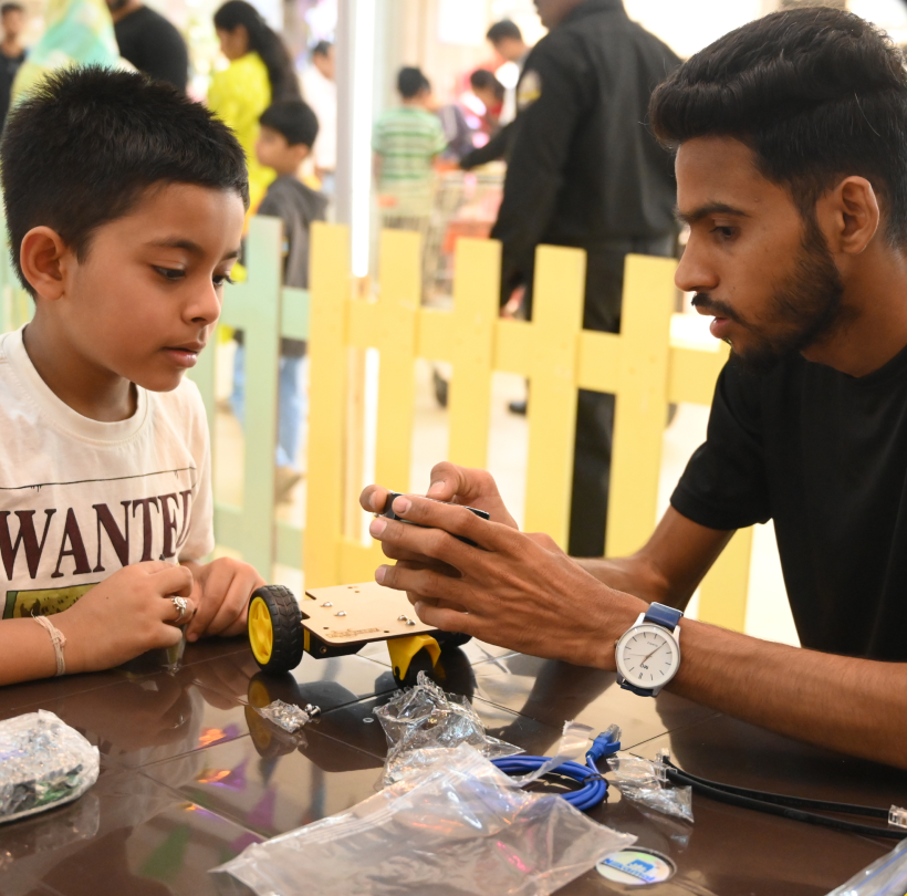 In frames — trainer helping a child with a robot chassis on a school visit